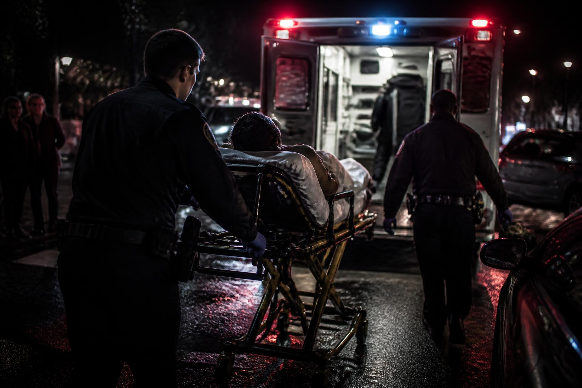 Paramedic crew loading a patient into an ambulance on a wet New York street at night