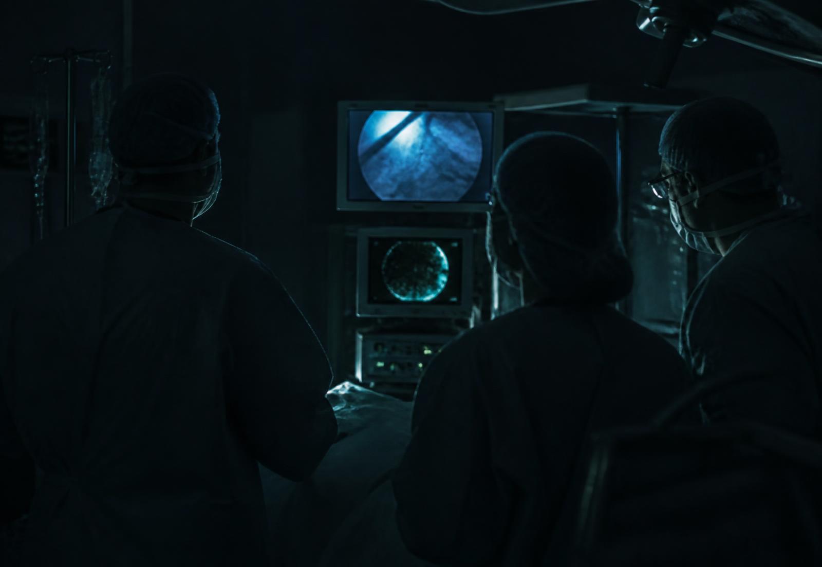 Surgical team working beside monitoring displays in a darkened operating suite